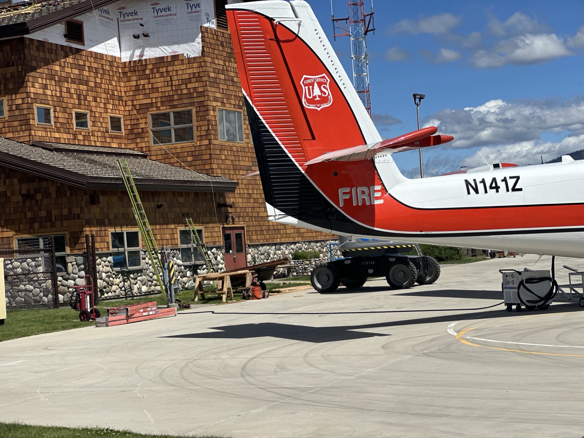 After photo of McCall Smoke Jumper Base — close-up of US Forest Service fire plane N141Z tail with FIRE markings and completed building behind