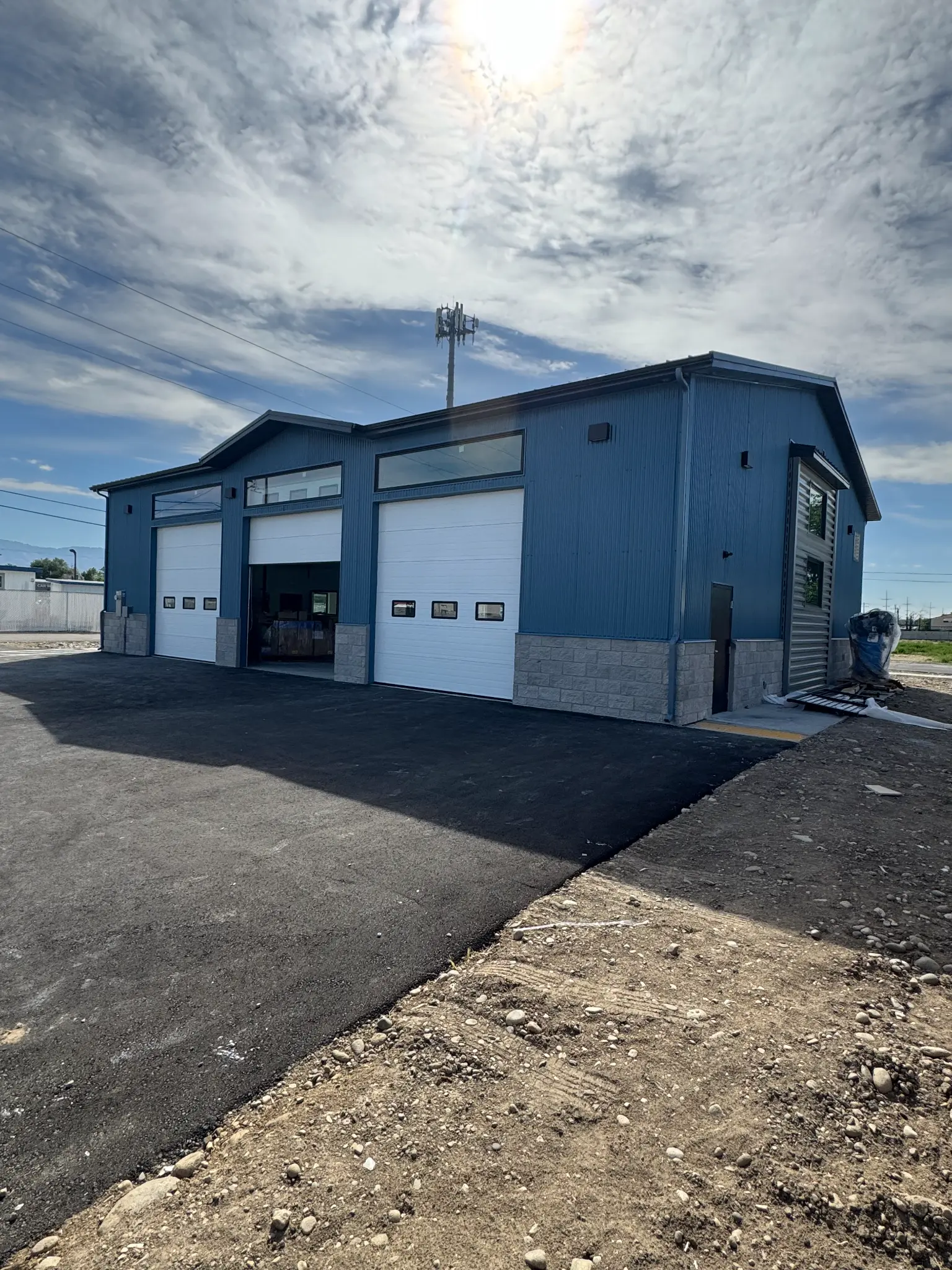 After photo of commercial building warehouse front with finished blue steel siding, two white roll-up garage doors, clerestory windows, and stone wainscoting