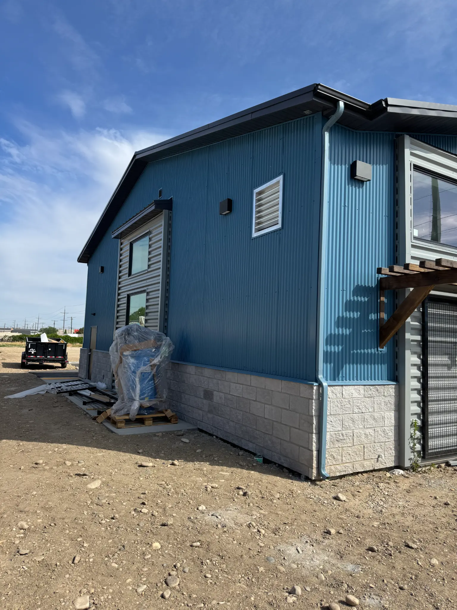 After photo of commercial building warehouse side wall with finished blue steel siding, two windows, stone wainscoting, and corner transition to gray office section