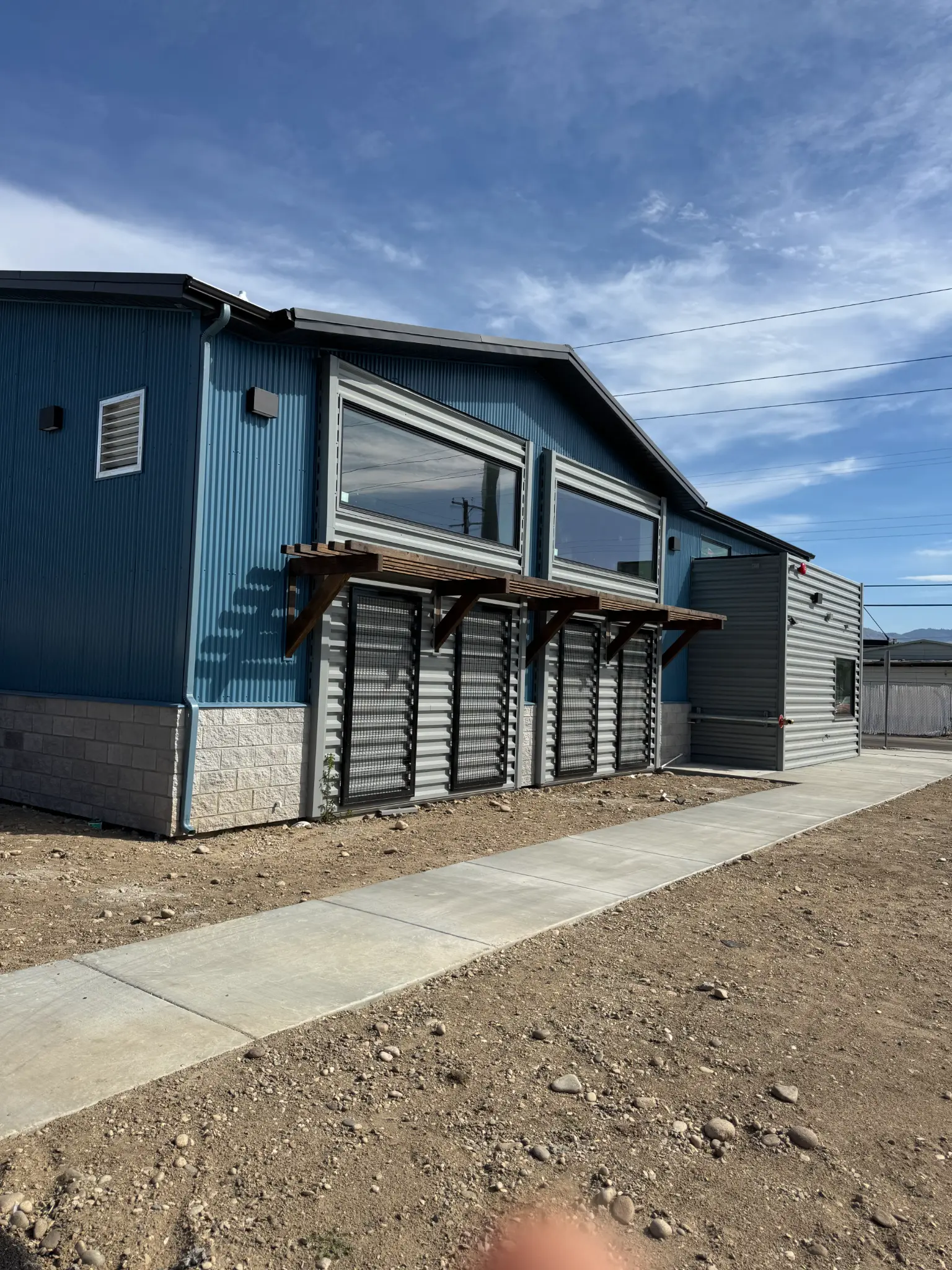 After photo of commercial building office wing side wall with finished gray corrugated steel siding, 3 panoramic windows, and installed wood canopy brackets