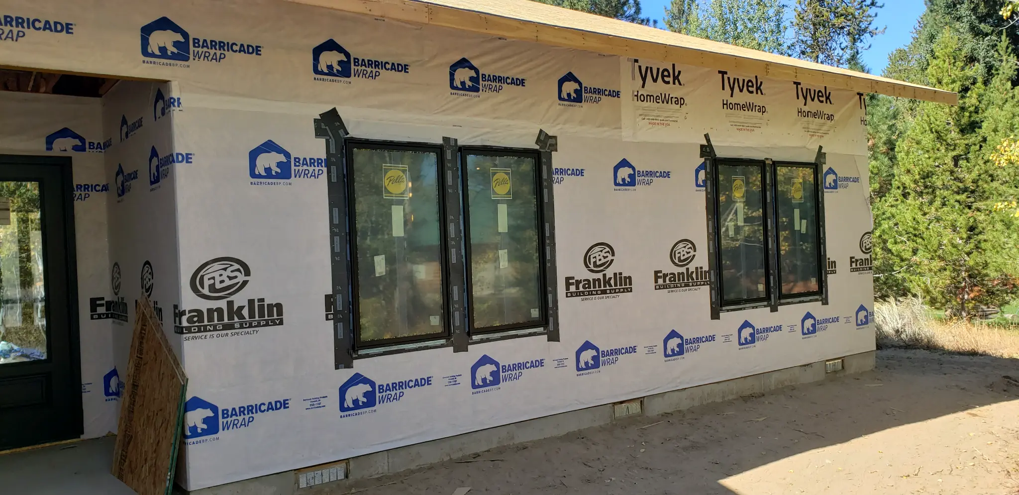 Before photo of House 1 during HBSI siding work with housewrap, exposed openings, and installed windows before the finished exterior siding